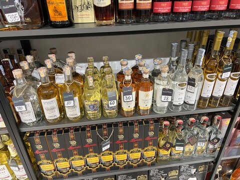 Shelves filled with various bottles of traditional Georgian wine, chacha, and spirits with price tags in a local liquor store in Batumi, Georgia, 2023 