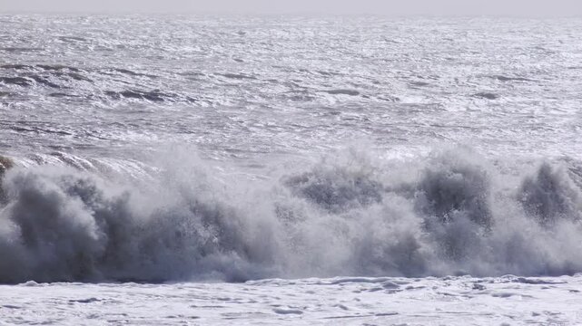 Strong surf and foamy waves roll toward the shoreline on a windy day. Wide seascape footage with natural light and sea spray.