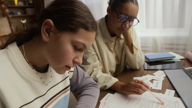 Caucasian teen student writing in notebook attentively while her tutor sitting near her and watching