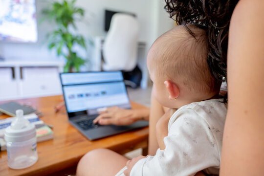 Mother sitting and working remotely with her baby on her lap. Work-life balance concept.