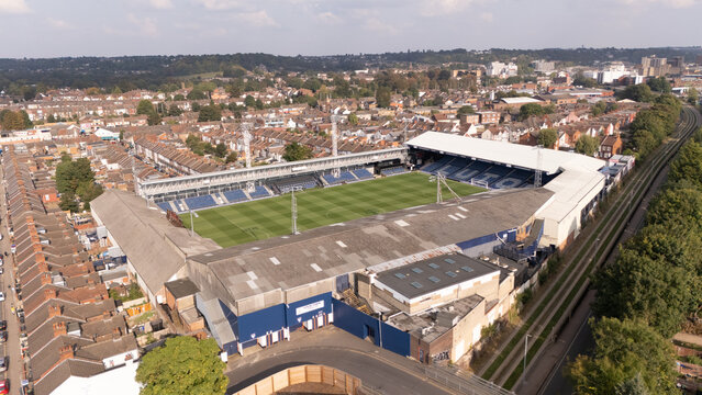 Luton, United Kingdom - 20 September 2024: Aerial view of a stadium nestled in the heart of Luton, surrounded by terracotta rooftops and lush green trees, bisected by a railway line.