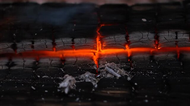 Close-up of Charred Wood Surface with Intense Orange Embers and Ash Residue
