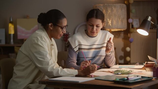 Static shot of young tutor watching teen student who solving math problem and explaining solution during personal lesson at home