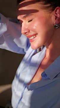 A woman waves happily while sitting in a bright room with sunlight coming through