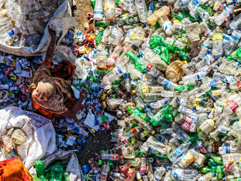 Aerial view of a worker amidst a sea of discarded plastic bottles, a stark contrast of human effort against overwhelming waste, Chattogram, Chittagong Division, Bangladesh.