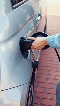 Woman is plugging electric vehicle for charging car battery at parking. Slow motion.