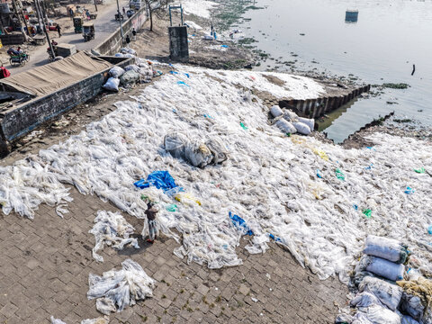 Aerial view of a vast expanse of discarded plastic waste creating a stark white contrast against the dark Buriganga River, Dhaka, Dhaka Division, Bangladesh.