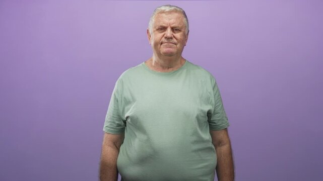 Man in light green tshirt with face shifting from closed eyes to gentle smile, arms relaxed at sides, standing against a purple studio wall; quiet contentment.
