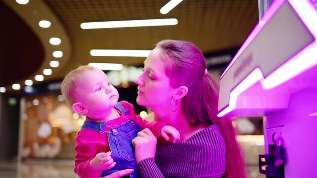 A mother shares a joyful moment with her baby in a vibrant, colorful setting, enjoying interactive technology and creating lasting memories together.