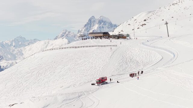 Aerial view Upper lift station at Tetnuldi ski resort, chairlift towers, groomed pistes, snowcat, groups of skiers, Caucasus mountain peaks, clear sky winter tourism concept