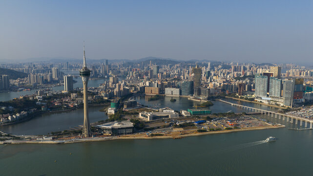 Cotai, Macao - 18 February 2026: Aerial view of the Macau Tower piercing the skyline, its gleaming white structure contrasting with the city's vibrant buildings and the tranquil waters below.