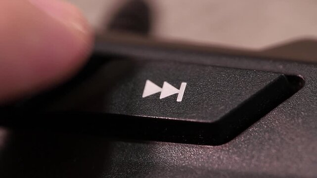 Skipping to the next song or video on a computer keyboard, macro shot of human finger clicking forward button