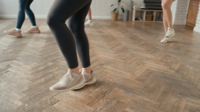 Low angle tilt-down shot of group of women dancing to warm up before exercising in spacious fitness studio room