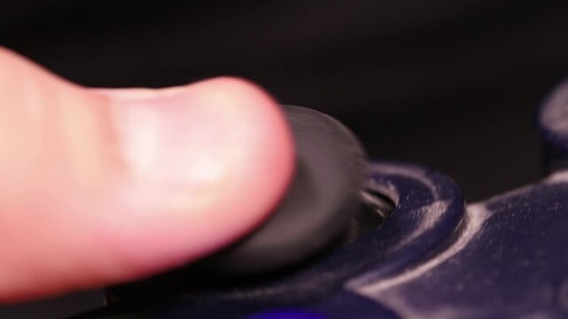 Macro shot of a child's thumb controlling a grimy analog joystick on a game controller.