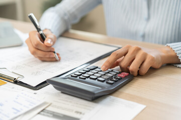 Fototapeta premium Stressed person asian young employee woman hand using calculator to calculate expenses of monthly and checking expenses from bill, receipt on table at home. Business and finance of banking concept