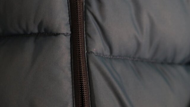 Opening a zipper on a dark puffer coat, close-up of fingers pulling down the slider.