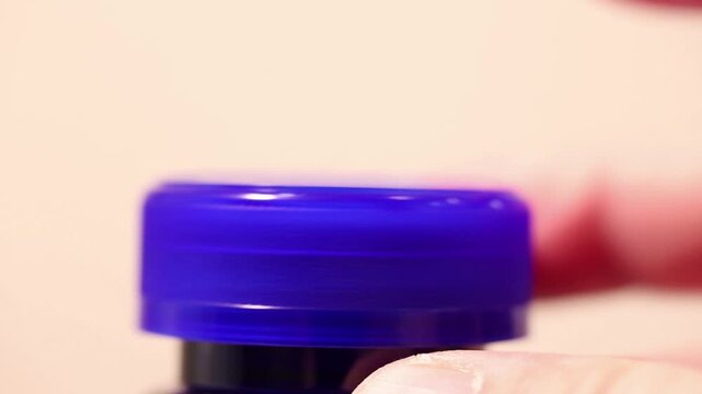 Macro close-up of a hand screwing on a blue plastic bottle cap.