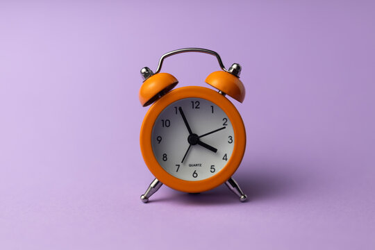 Retro orange alarm clock with bells on a pastel purple background, studio shot