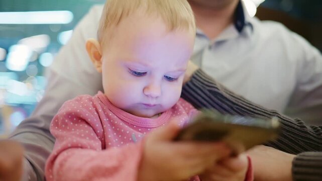 Captivated Baby Engaged with Smartphone: A Tender Moment of Modern Technology and Early Development in a Safe Environment with Family Surroundings