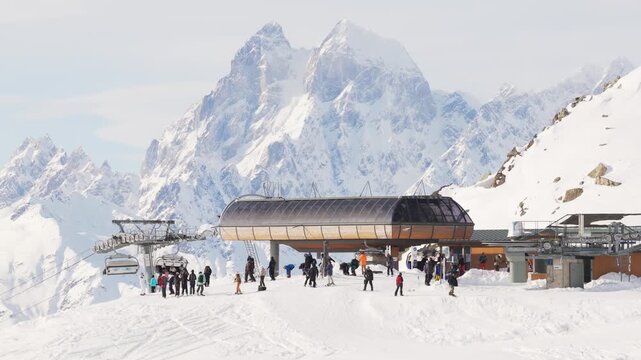 Aerial panoramic view crowded Tetnuldi upper lift station with skiers and snowboarders, chairlift terminal on snowy ridge, Ushba peak towering behind, Caucasus winter tourism concept