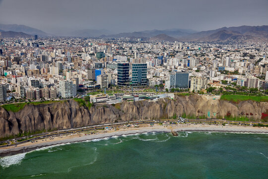aerial photograph showcasing the unique architecture of the Larcomar shopping mall, built directly into the cliffs of the Costa Verde. The image captures the dense urban landscape of the Miraflores