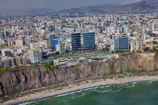 aerial photograph showcasing the unique architecture of the Larcomar shopping mall, built directly into the cliffs of the Costa Verde. The image captures the dense urban landscape of the Miraflores
