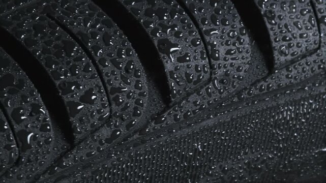 Wheel Tread Pattern After Rain. Wet tire spinning on a black background close-up. It is covered with sparkling water drops