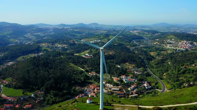 Scenic Aerial view of wind turbine over the small european town.  Windmill for energy production on beautiful blue sky. Close up view to the wind power turbine generating clean renewable energy.