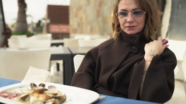 Stylish mature woman dining alone at terrace restaurant. Concept of self care, independence, emotional balance and confident lifestyle of a modern woman enjoying quiet time.