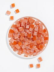 Plate of orange Turkish delight cubes with scattered pieces on white background, sweet candy, minimal food still life, studio shot