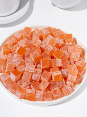 Plate of orange Turkish delight cubes on white background, sweet snack, food still life, studio shot, candy dessert