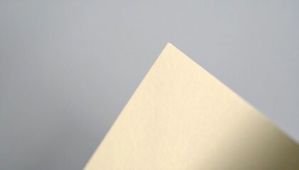 회색 배경 위에 놓인 베이지색 종이의 날카로운 삼각형 모서리를 근접 촬영한 미니멀하고 추상적인 이미지로 깔끔한 디자인 요소와 넉넉한 여백을 제공하여 세련된 분위기를 연출합니다.