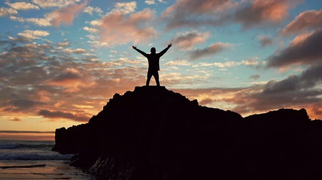 Man stands on a rock  is looking distance during beautiful summer sunset. Human with raised hands looks to the sun over horizon in morning while sunrise. Freedom.