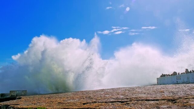 Large ocean waves crash about the  pier. Slow motion - ocean waves splashes. Beautiful sea with crashing waves about wharf on summer sunny day.  Sea water is  crashing on dock creating huge splashes