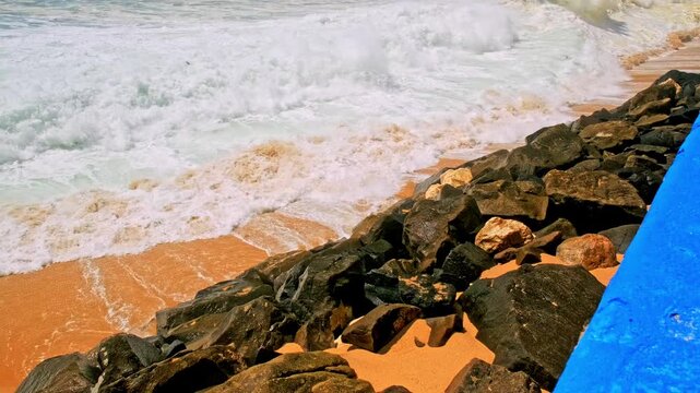 Large ocean waves are rolling on sandy beach during tide.   Beautiful azure ocean on summer sunny day in touristic place Ericeira, Portugal.  Slow motion - Powerful sea storm with huge waves
