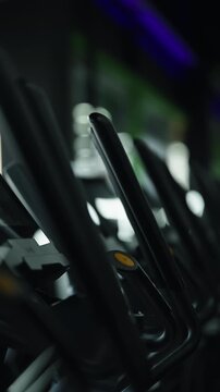 Row of cardio exercise machines in a modern gym, with sleek black handlebars, yellow controls, captured in moody lighting with a shallow depth of field