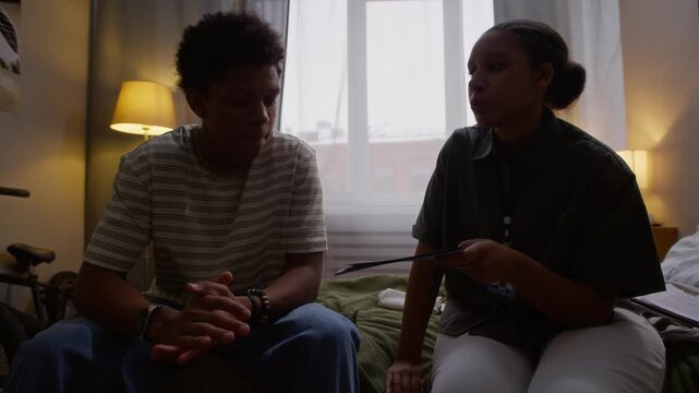 Medium long handheld shot of young African American female social worker giving brochure with social assistance programs to teenage boy during home visit