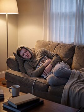Crohn&rsquo;s Disease: Professional photography, young man curled up on a sofa clutching his abdomen in pain, heating pad visible, pale complexion, soft evening domestic lighting.