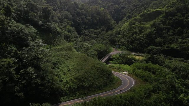 Aerial push in above twisty road in Costa Rica Rainforest tilt up to jungle mountains