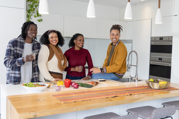 African American friends chatting and preparing salad on wooden island in modern kitchen with knife