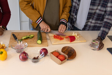 Three adults chopping veggies at kitchen counter, center wearing mustard jacket using chef's knife © wavebreak3
