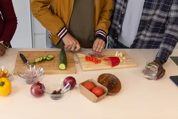 Fotobehang Koken Three adults chopping veggies at kitchen counter, center wearing mustard jacket using chef's knife  © wavebreak3