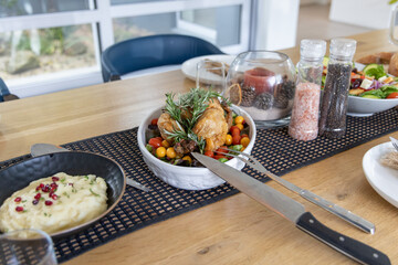 Whole roasted chicken resting on bed of cherry tomatoes and rosemary, carving knife pointing nearby