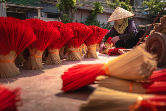View of a woman in traditional conical hat arranging bundles of vibrant red incense sticks, a sensory explosion of color and aroma, Ung Hoa, Ha Noi, Vietnam.