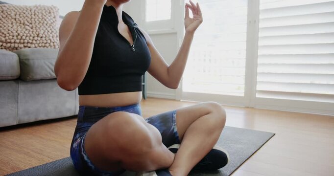 African American woman sitting on yoga mat at home, zipping black crop-top, forming mudra for calm