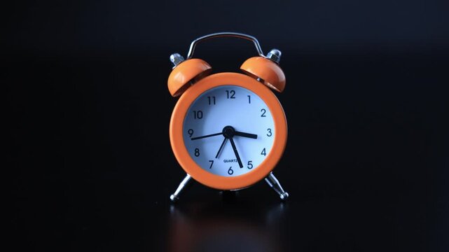 Retro orange twin bell alarm clock on a dark reflective surface
