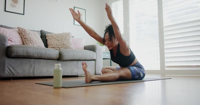 African American woman inhaling, hinging forward, stretching hamstring on mat in gear, green bottle