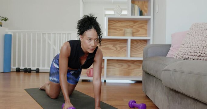 African American woman bracing left hand pulling purple dumbbell to torso on black mat for strength