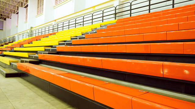 Rows of empty colorful orange and yellow stadium seats in Indoor sports arena bleachers or grandstand background for spectators. perspective side view with copy space