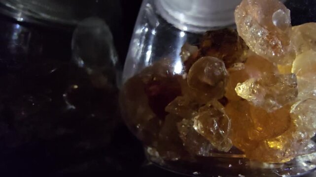 Close-up of glass jars containing high-quality Gum Arabic and Frankincense (Luban) crystals. The shot highlights the organic texture and amber-gold transparency of these natural resins.